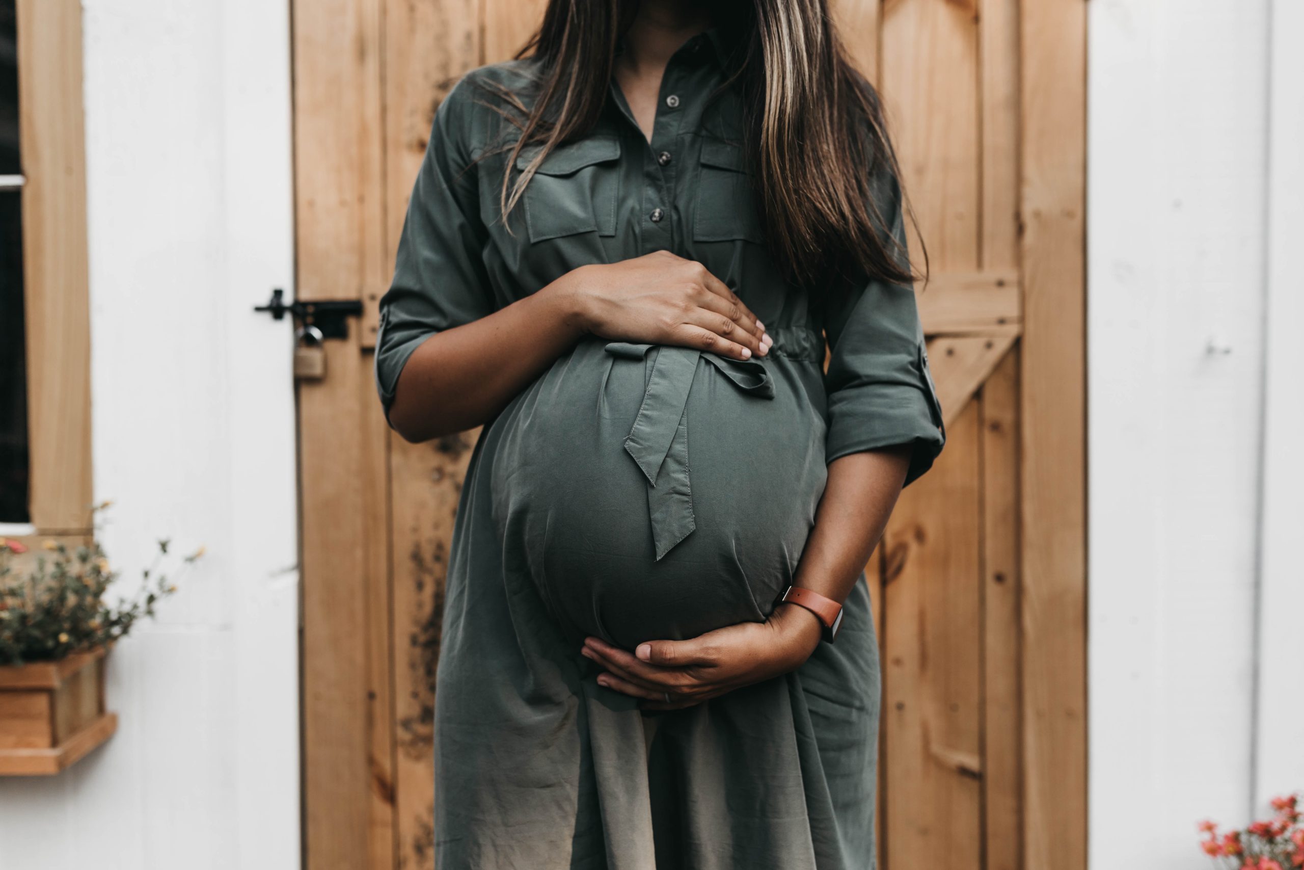 woman with healthy long brown and blonde hair cradles pregnant belly.