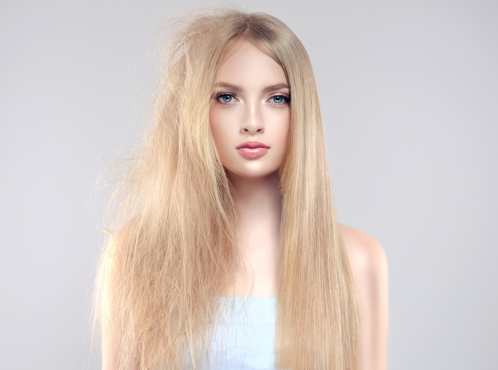 Caucasian woman with long blonde hair looks at camera, and has frizzy, damaged hair on one side of hair and smooth, sleek hair on the other side of her hair.