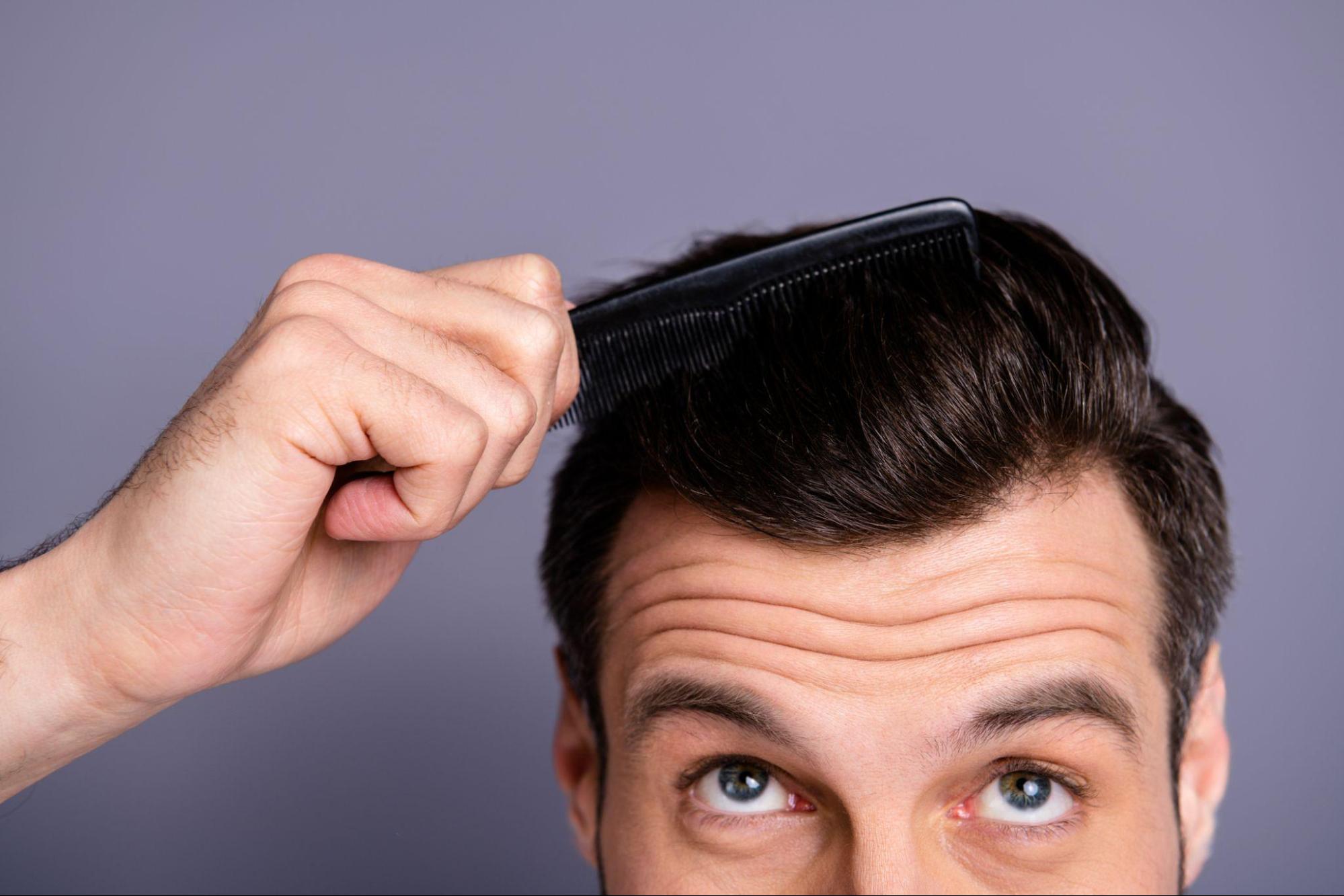 Man learns about preventing hair loss and combs through thick brown hair while looking towards camera.